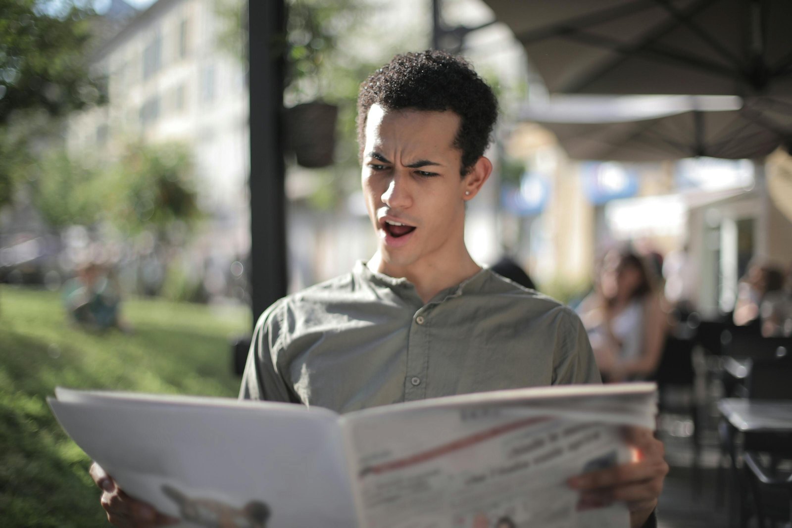 A young man is surprised while reading a newspaper at an outdoor cafe.